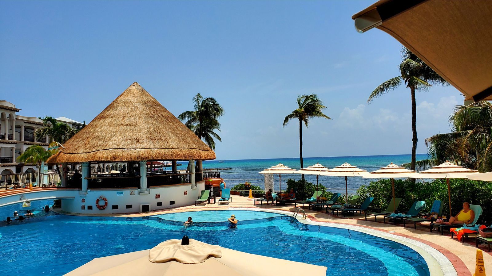 Resort swimming pool with a thatched palapa bar and sea view